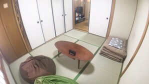 A tatami mat room with a futon bed, a small table, and a television in the background. - Hanazono Kita Terrace House (Osaka)