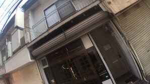 A building with a closed shutter, a balcony with metal railings, and air conditioning units on the facade. - Hanazono Kita Terrace House (Osaka)