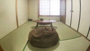 A traditional Japanese room with tatami flooring, a tatami mat table, a futon bed, and sliding doors. - Hanazono Kita Terrace House (Osaka)