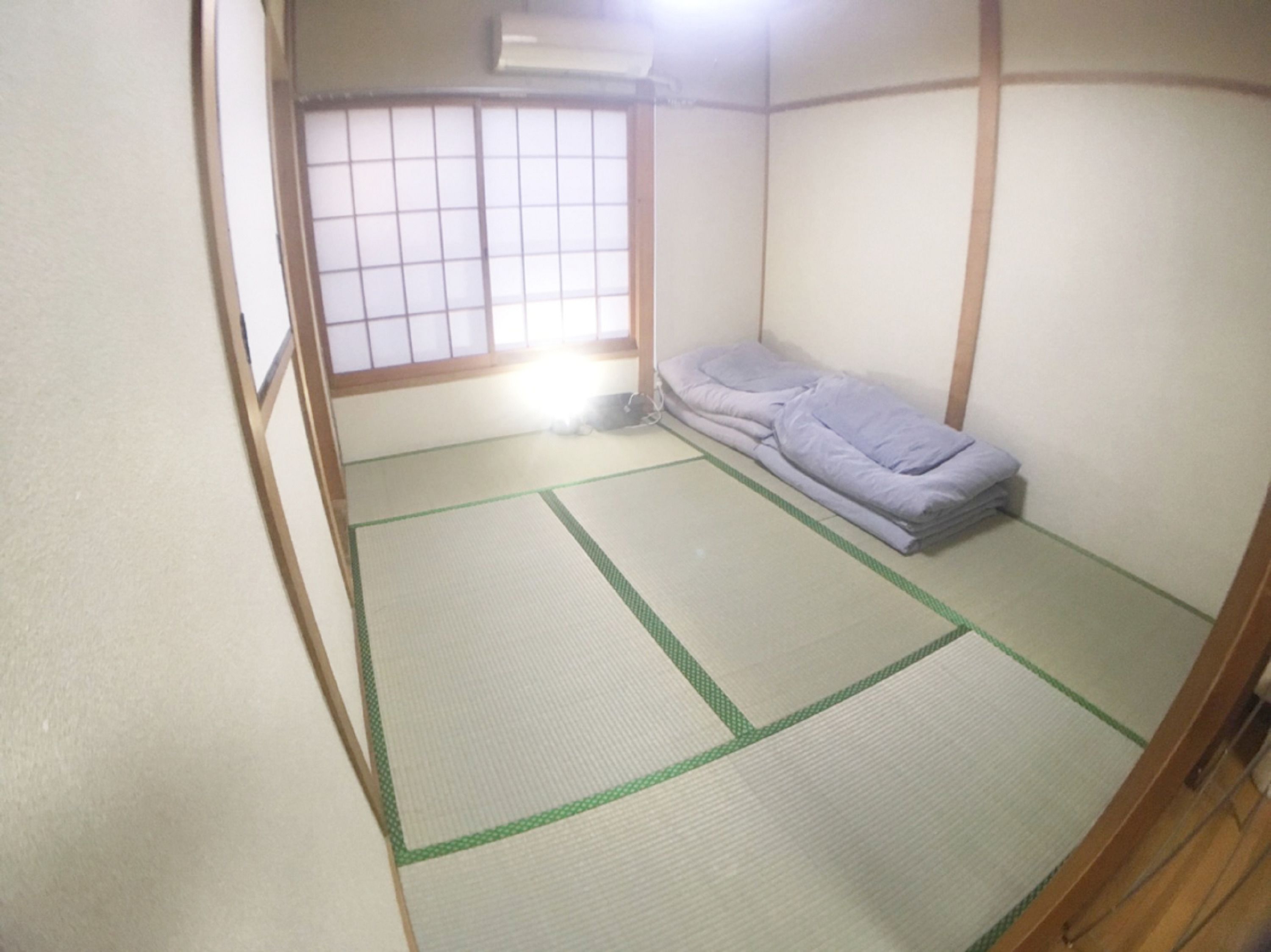 A traditional Japanese room with tatami flooring, a futon bed, and a shoji screen window.