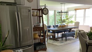 Een moderne keuken met een roestvrijstalen koelkast, houten kastjes en een eethoek met een tafel en stoelen.
