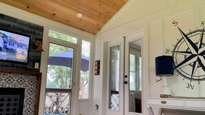 Een woonkamer met een televisie, een open haard, een groot raam en een kompas als wanddecoratie.