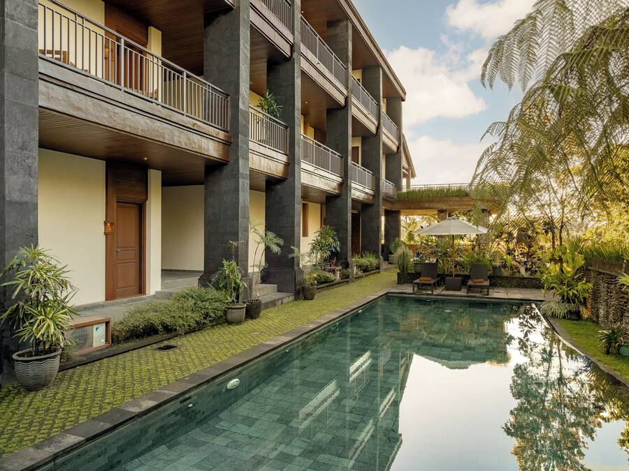 Ein Pool mit spiegelglatter Wasseroberfläche, ein Gebäude mit Balkonen und umliegendes Grün.