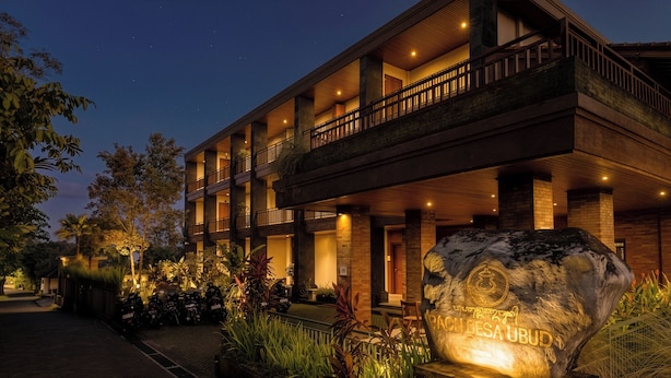 A multi-story hotel with a stone facade, outdoor seating, and a large rock with inscriptions. - Paon Desa Ubud Hotel (Ubud)