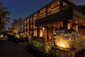 A multi-story hotel with a stone facade, outdoor seating, and a large rock with inscriptions.