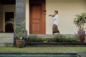 A person carrying a large wooden object, a building entrance with a wooden door, and potted plants.