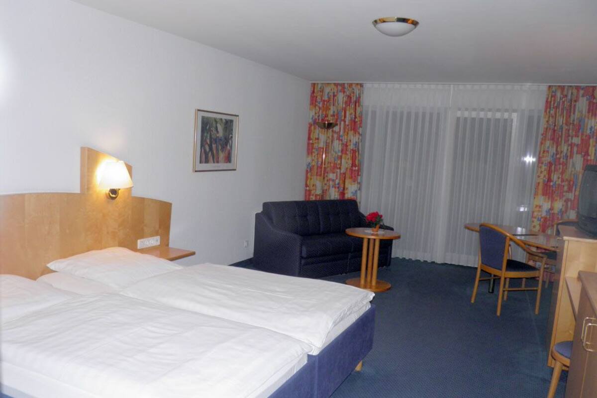 A hotel room with a large bed, a desk, a chair, and a small table.