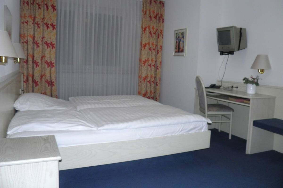 A hotel room with a bed, a desk with a chair, a television, and a lamp.