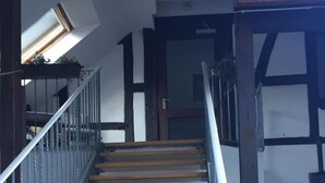 Una escalera de madera con barandales de metal, que conduce a un rellano con una puerta y una ventana.