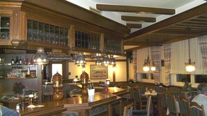 Un restaurante con barra de madera y cabinas, techo alto con vigas a la vista y lámparas colgantes.