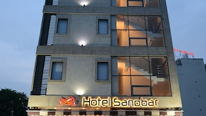 A multi-story hotel with a modern design, featuring a prominent entrance with a closed shutter and a sign that reads "Hotel Sanobar." - Hotel Sanobar (Udaipur)