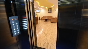An elevator interior with a control panel and a view into a lobby area featuring a sofa, a coffee table, and a television. - Hotel Sanobar (Udaipur)