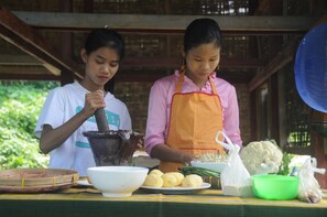 Two individuals preparing food at a table with various vegetables and cooking utensils. - Ngwe Saung Garden Guest House (Ngwe Saung)