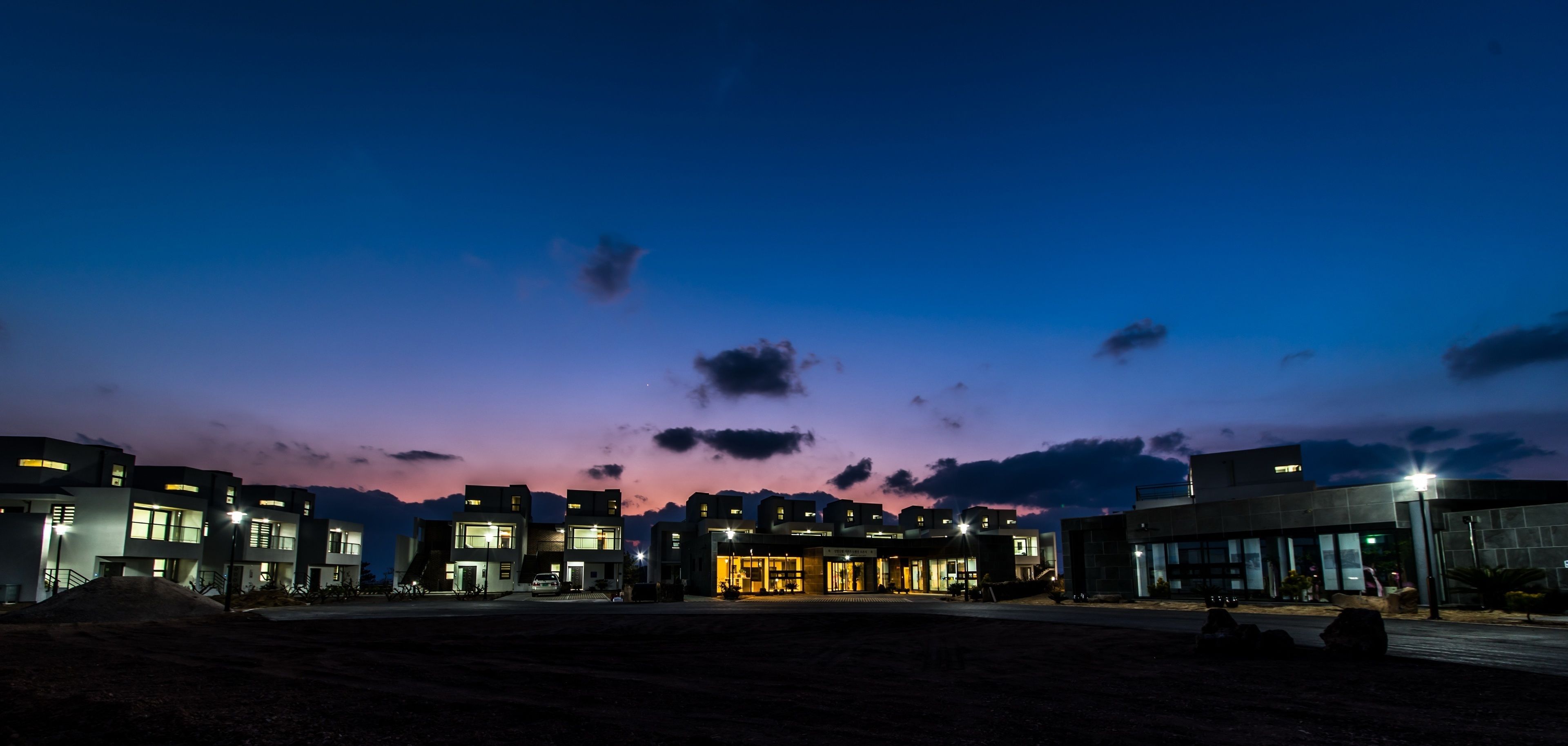 A modern building complex with multiple structures, including a central building with illuminated signage, surrounded by smaller buildings.