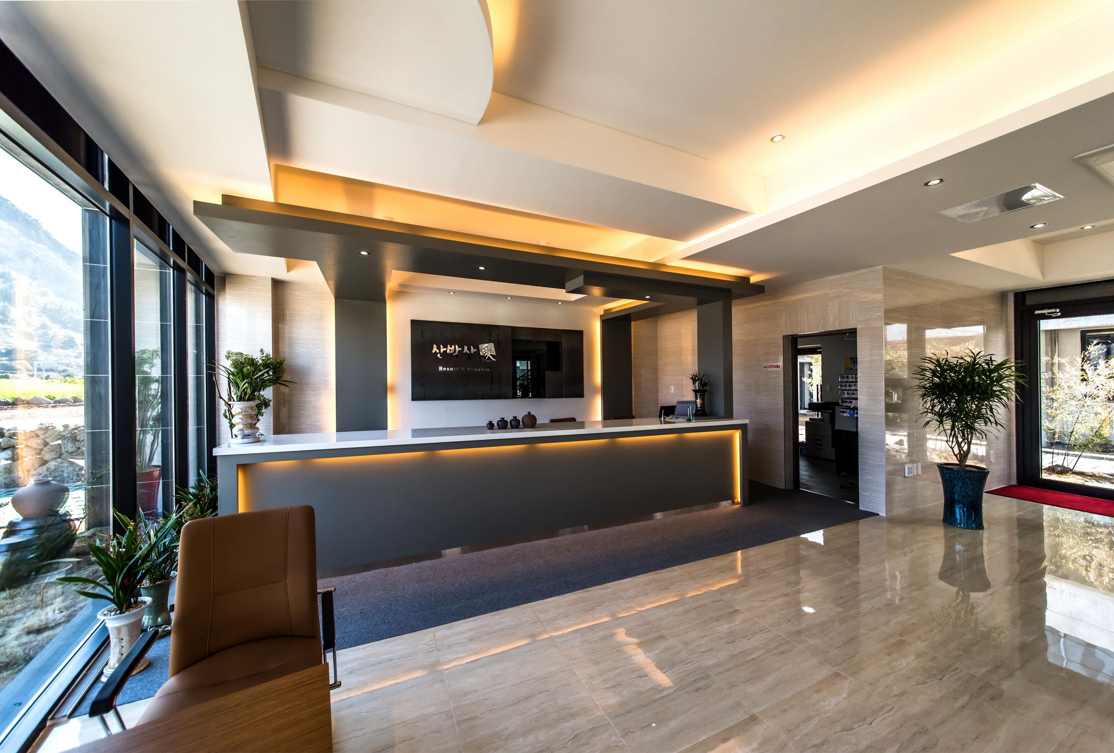A modern reception area with a sleek reception desk, potted plants, and a view through large windows.