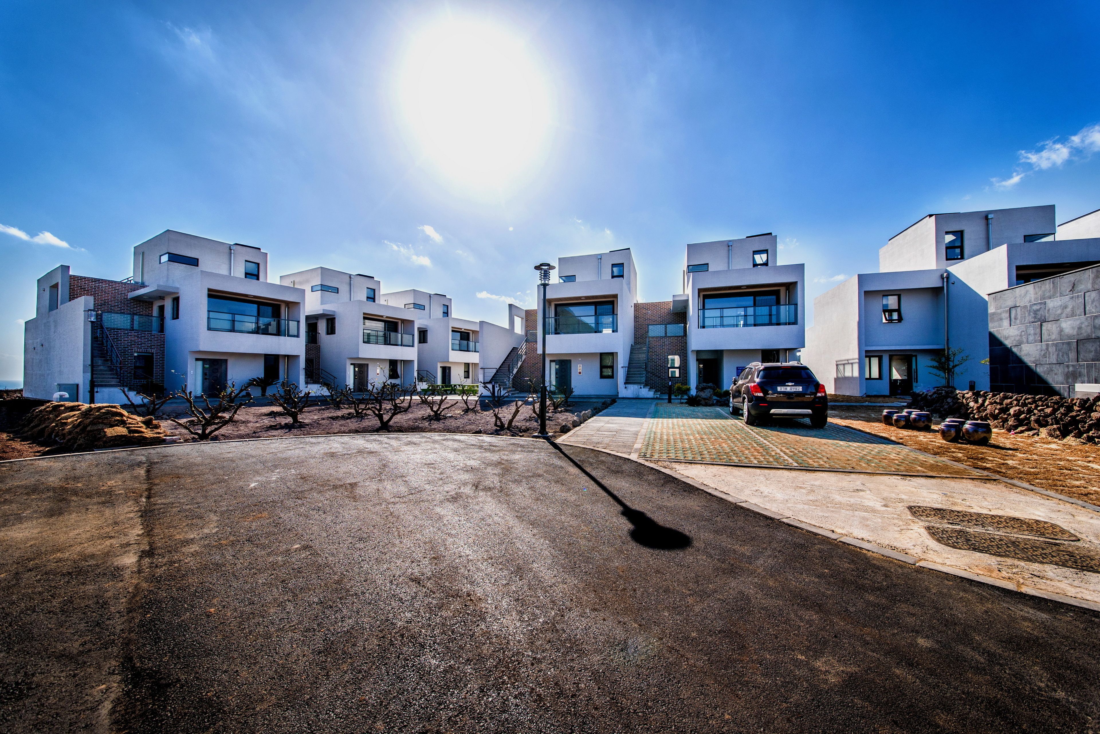 A modern residential complex with multiple apartment buildings, a paved driveway, and a parked car.