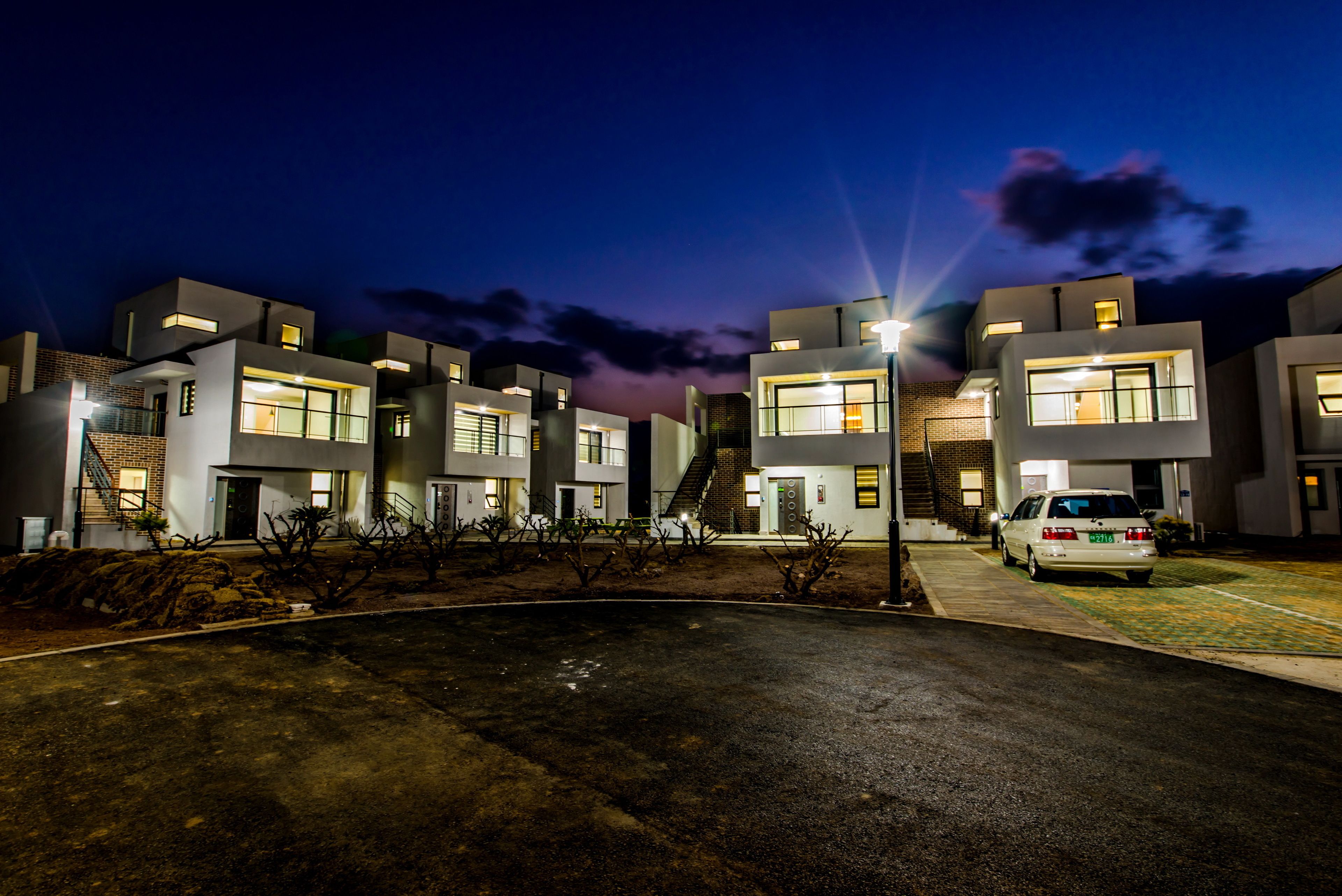 A modern building complex at night with illuminated windows and a car parked in front.