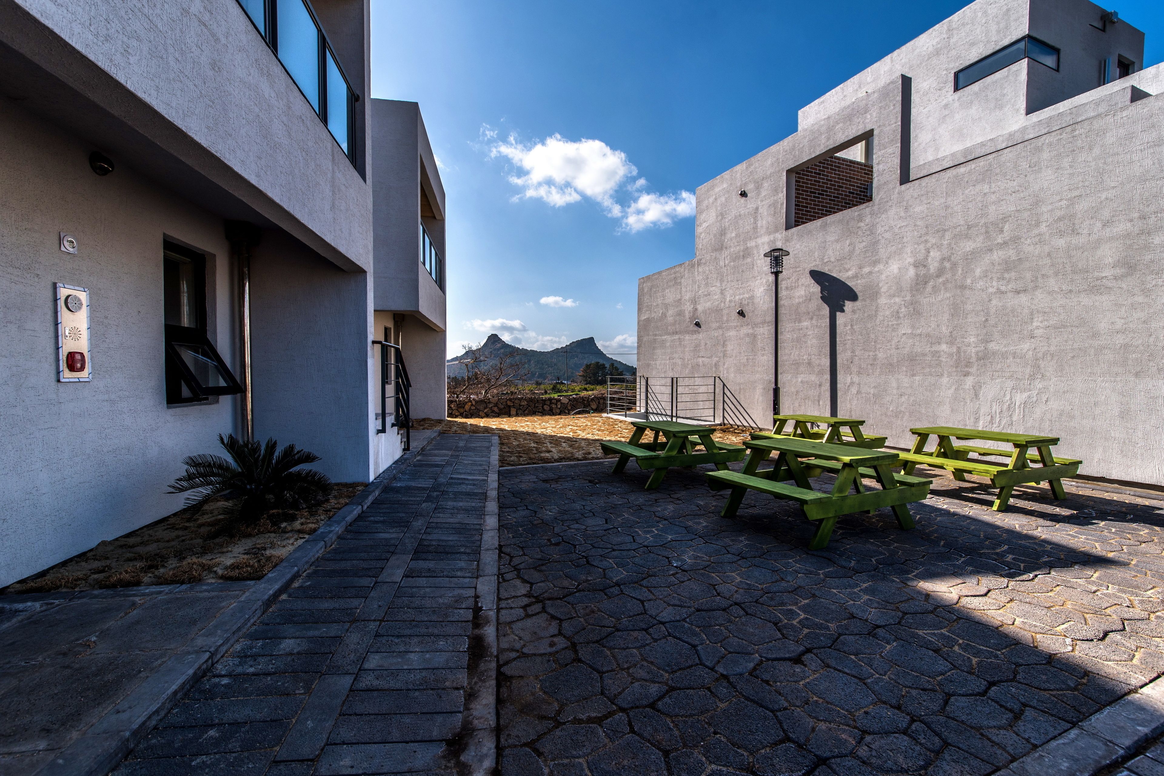 Un patio con un camino empedrado, mesas de picnic y un edificio de diseño moderno con vistas a la montaña al fondo.