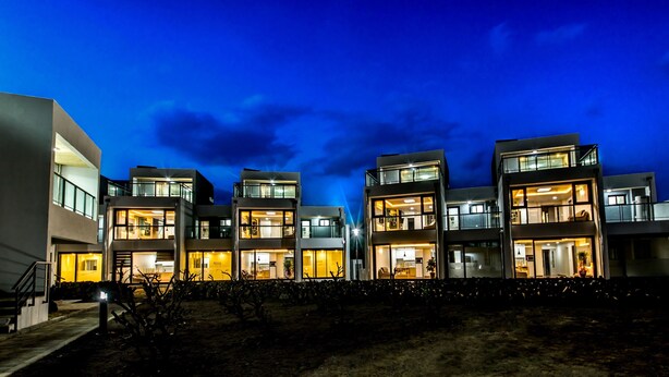 Un edificio residencial moderno de varios pisos con balcones y ventanas grandes, rodeado de áreas ajardinadas.