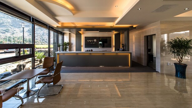 Un moderno hall de hotel con mostrador de recepción, zona de estar y grandes ventanales con vistas al exterior.