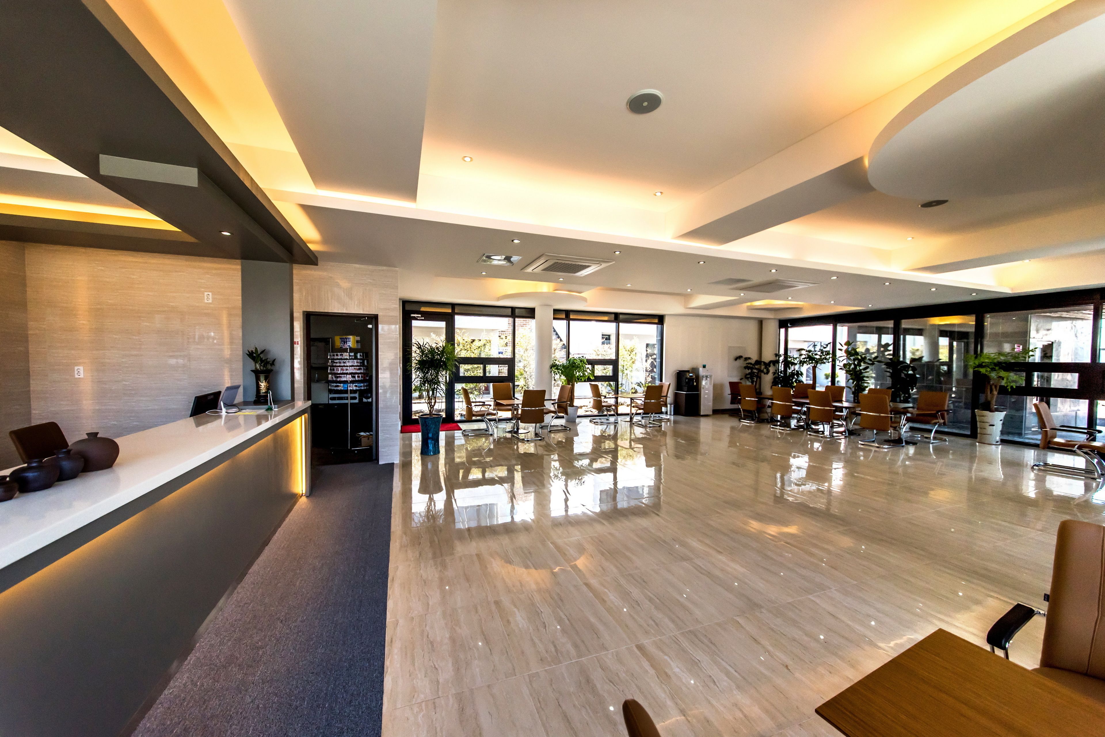 Un hall d’hôtel moderne doté d’un comptoir d’accueil, d’un espace salon et de grandes fenêtres laissant entrer la lumière naturelle.