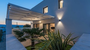 A modern house with a covered patio, a small garden with palm plants, and a view of the hills in the background. - Villa Bella Vista B - contemporary villa with a private pool near a beach by MyWaycation (Linardici)
