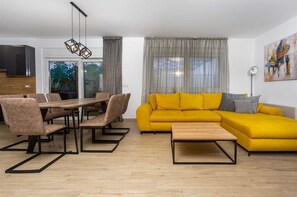 A modern living room with a yellow sofa, a wooden dining table with chairs, and a kitchen area visible through a glass door. - Villa Bella Vista B - contemporary villa with a private pool near a beach by MyWaycation (Linardici)