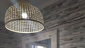 A room with a rustic wooden wall, a white console table with a mirror, a hanging light fixture, a potted plant, and a wooden chair. - V Barcelona Hostal (Barcelona)