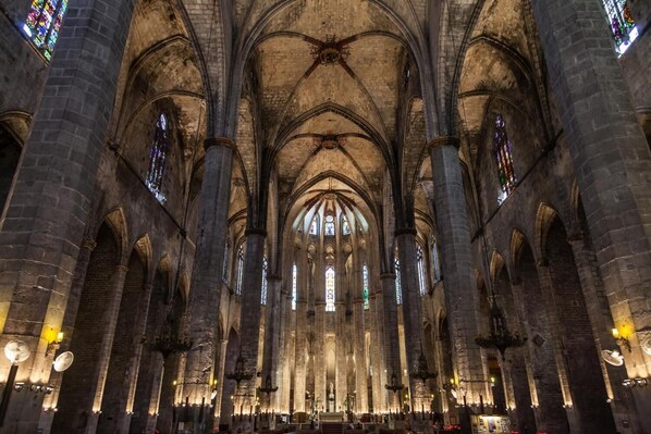 Interior de una catedral con altos techos abovedados, amplias vidrieras y un pasillo central que conduce a un altar.