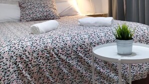 A neatly arranged bedroom with a bed, pillows, a bedside lamp, a small round table with a plant, and a window with curtains. - V Barcelona Hostal (Barcelona)