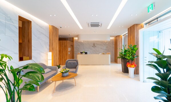Un vestíbulo moderno de hotel con una recepción, un sofá, una mesa de centro y plantas en macetas.