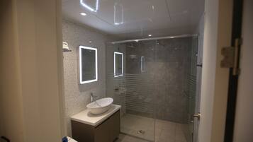 A modern bathroom with a glass-enclosed shower, a white sink, and a mirror with integrated lighting.