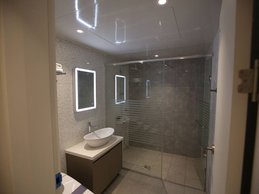 A modern bathroom with a glass-enclosed shower, a white sink, and a mirror with integrated lighting.