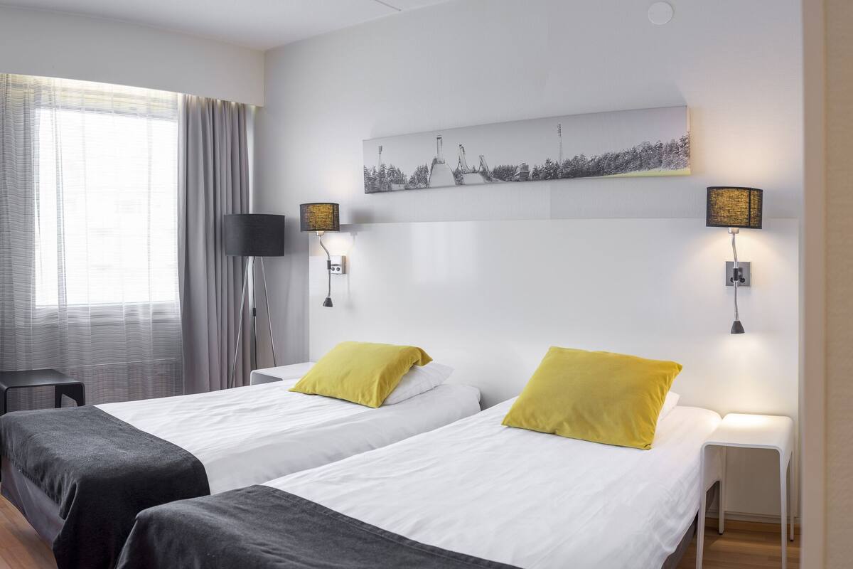 A hotel room with two beds, a desk, a chair, a TV, and a painting on the wall.