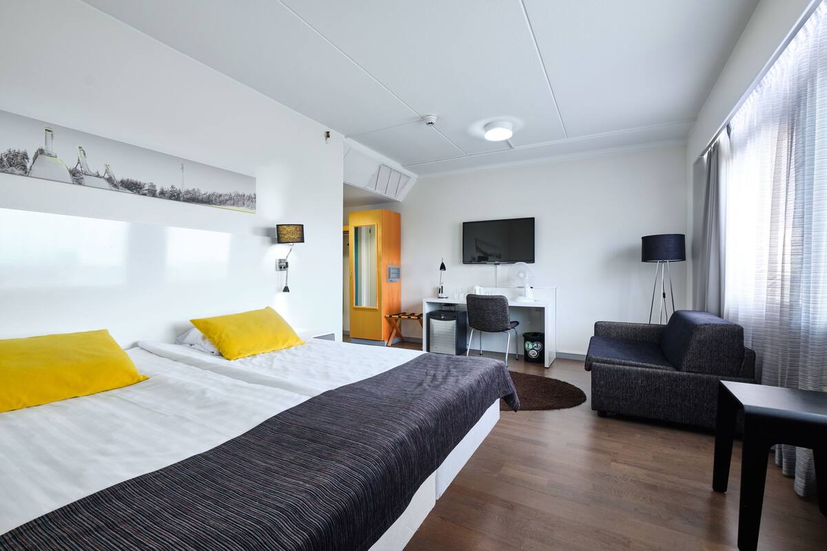 A modern hotel room with a large bed, a desk, a sofa, and a TV.