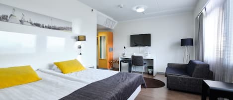A modern hotel room with a large bed, a desk, a sofa, and a TV.