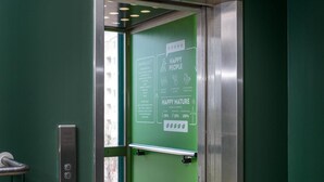 An elevator with a green interior and a sign promoting sustainability. - GreenStar Hotel Lahti (Lahti)