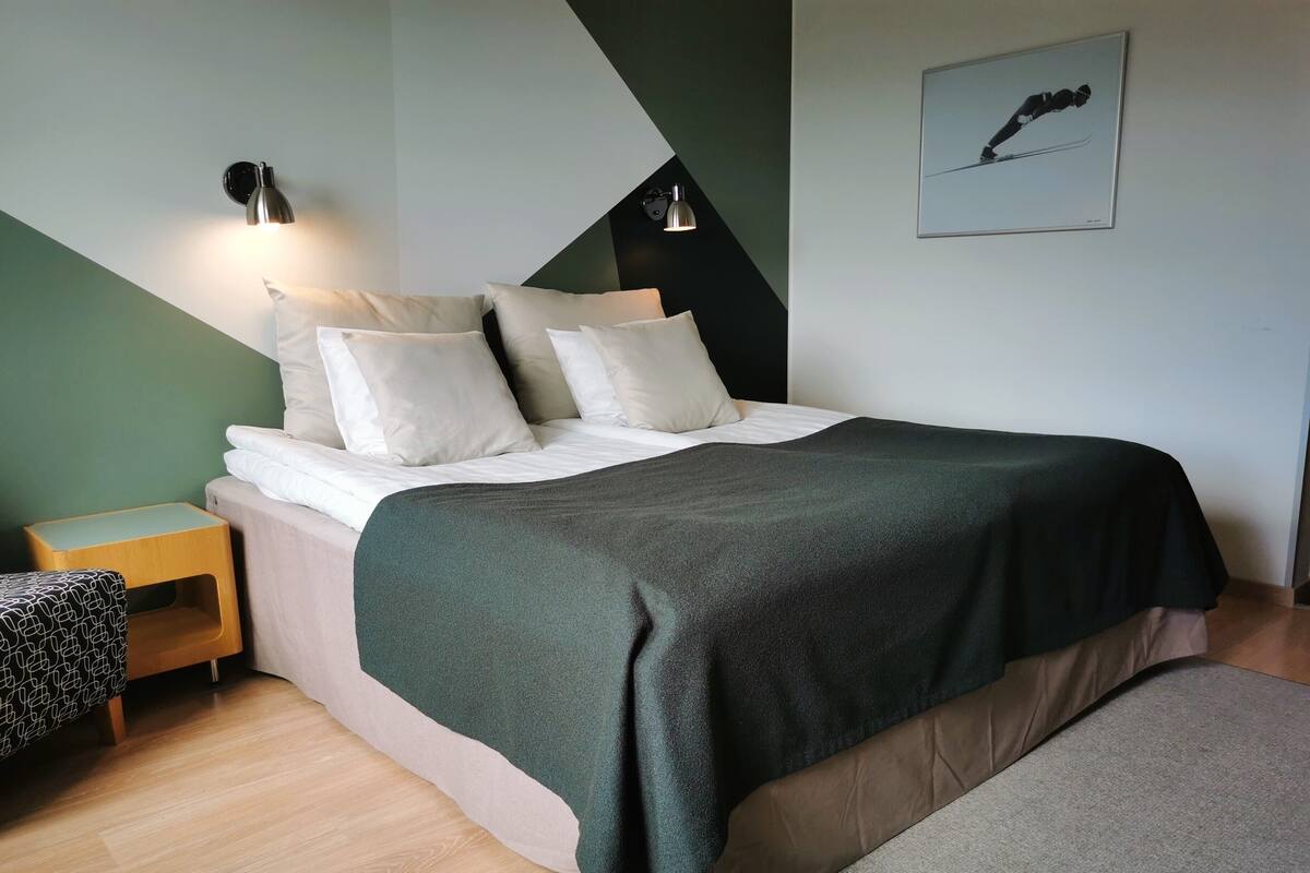 A modern bedroom with a bed, bedside tables, a green wall, and a framed picture.