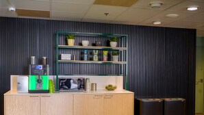 A kitchenette with a coffee machine, microwave, and storage cabinets. There are shelves with plants and kitchenware. - GreenStar Hotel Lahti (Lahti)