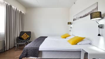 Moderni hotellihuone, jossa on sänky, tuoli, lamppu ja taulu seinällä.
