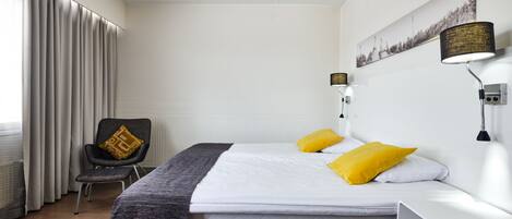 A modern hotel room with a bed, a chair, a lamp, and a painting on the wall.