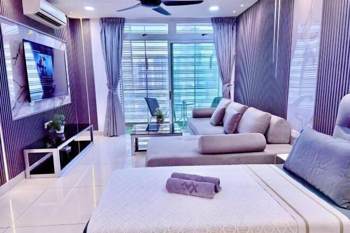 A modern hotel room with a large bed, a sofa, a TV, and a balcony with a view.