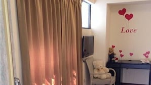 Quarto com uma janela grande, uma cadeira, um urso de pelúcia e uma parede decorada com um letreiro de 'Love' e corações.