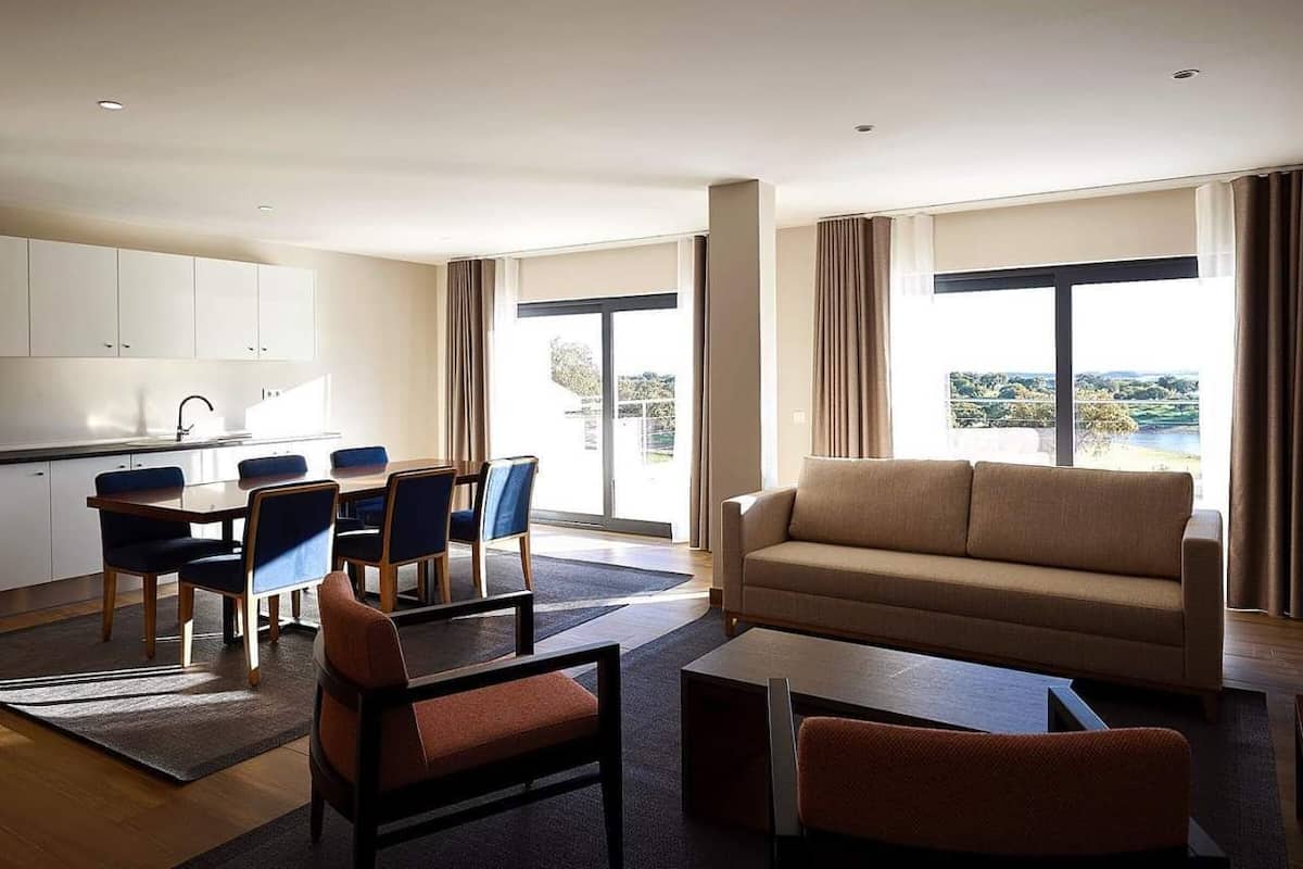 A modern living room with a sofa, coffee table, and chairs, a dining area with a table and chairs, and large windows with a view.