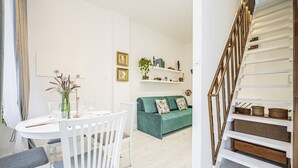 Una sala de estar moderna con un sofá verde, una mesa de comedor blanca y una escalera con barandillas de madera.