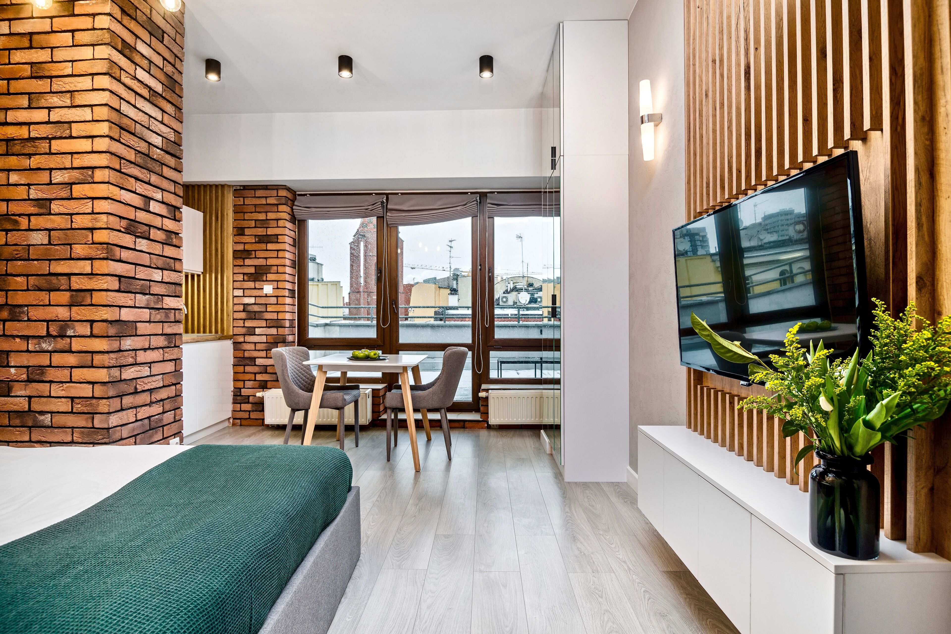 Una habitación moderna con un muro de ladrillo decorativo, un televisor grande, un comedor y vistas a la ciudad.