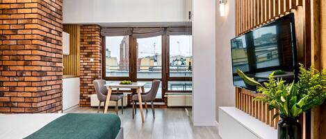 Una habitación moderna con un muro de ladrillo decorativo, un televisor grande, un comedor y vistas a la ciudad.