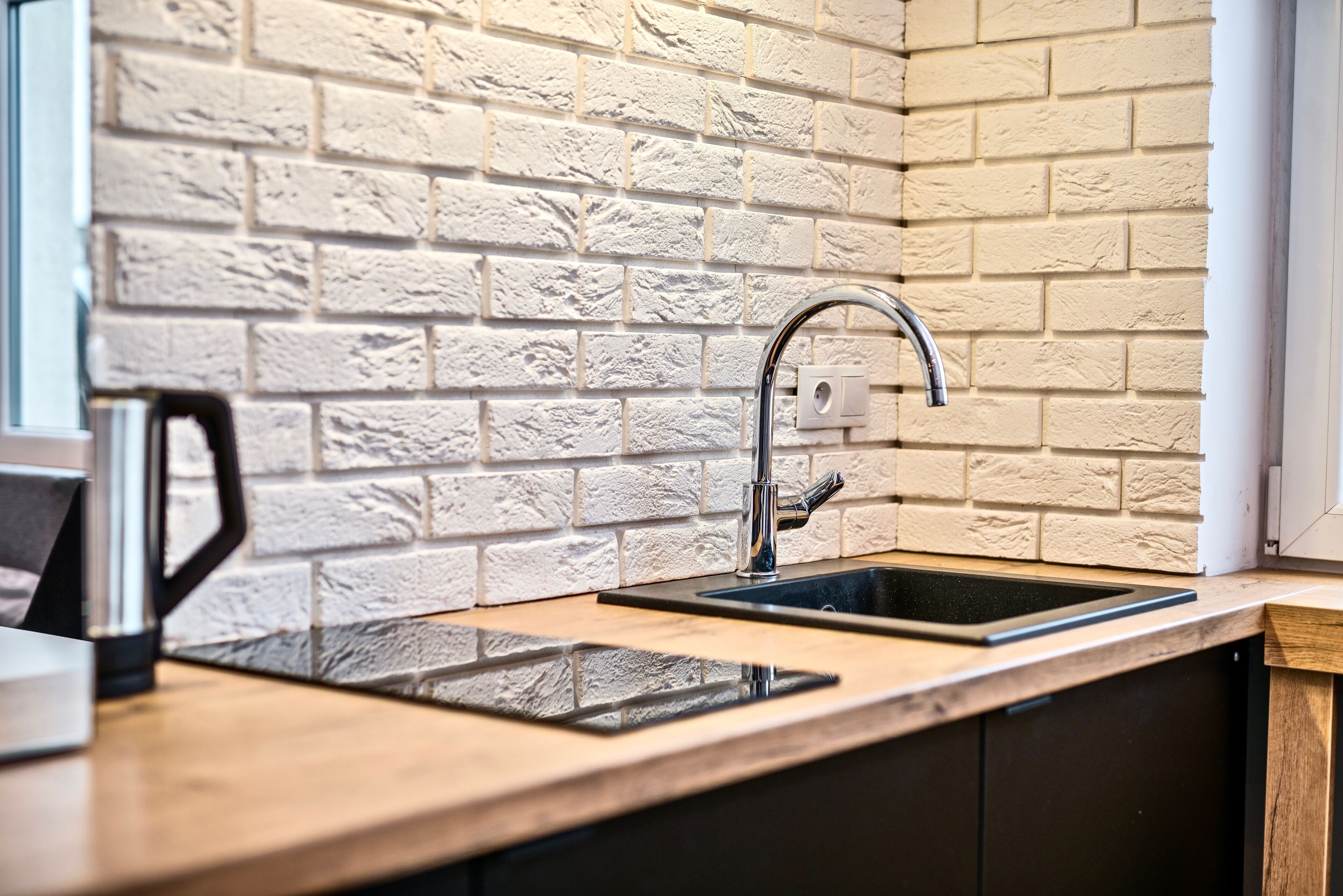 A kitchen with a brick wall backsplash, a stainless steel sink, and a modern faucet.