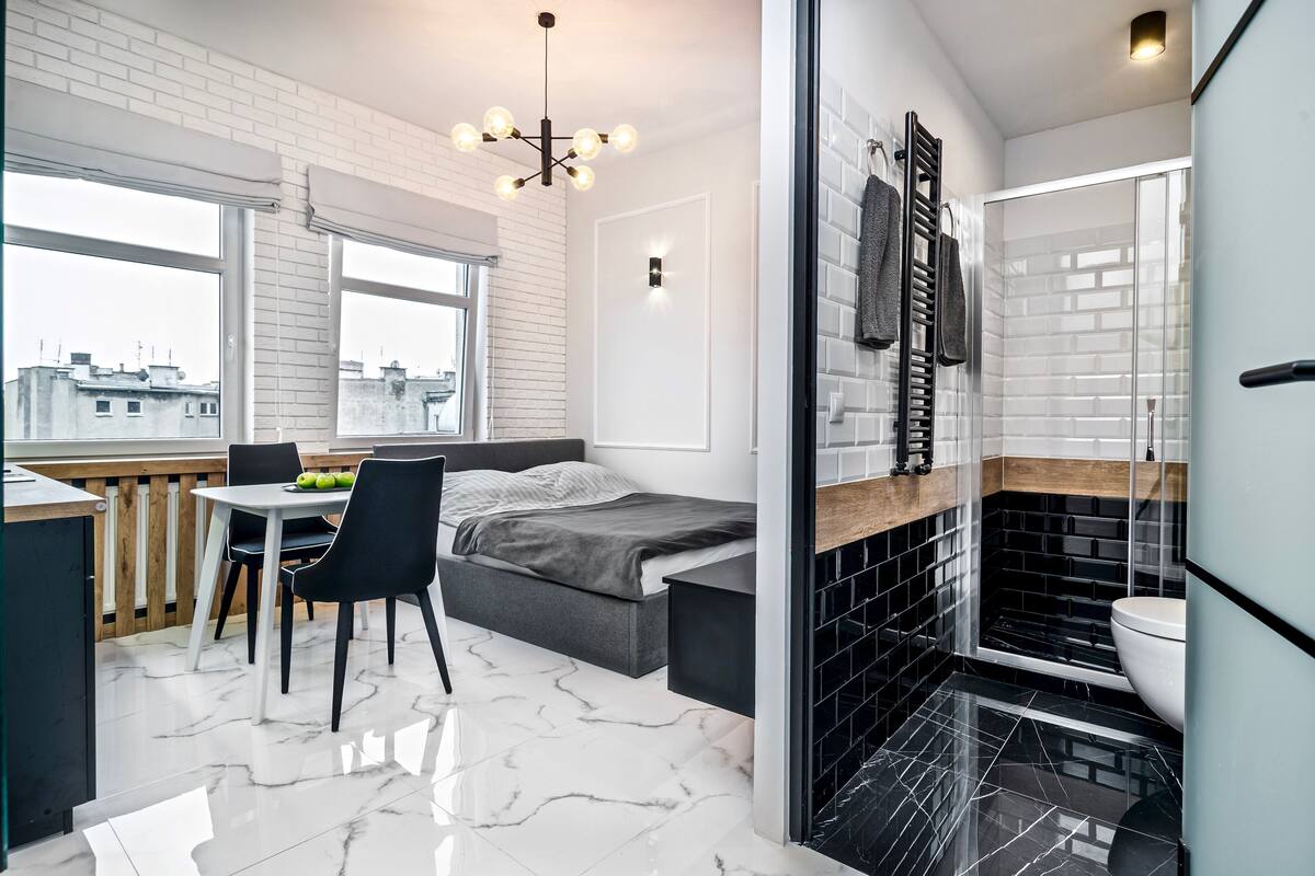 Une pièce de taille modeste comprenant un lit, une table à manger avec des chaises, un petit coin cuisine et une salle de bain avec douche et toilettes.