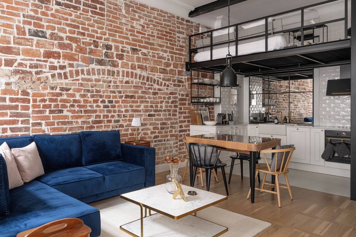 Un salon moderne avec un canapé bleu, une table à manger en bois et un mur en briques.